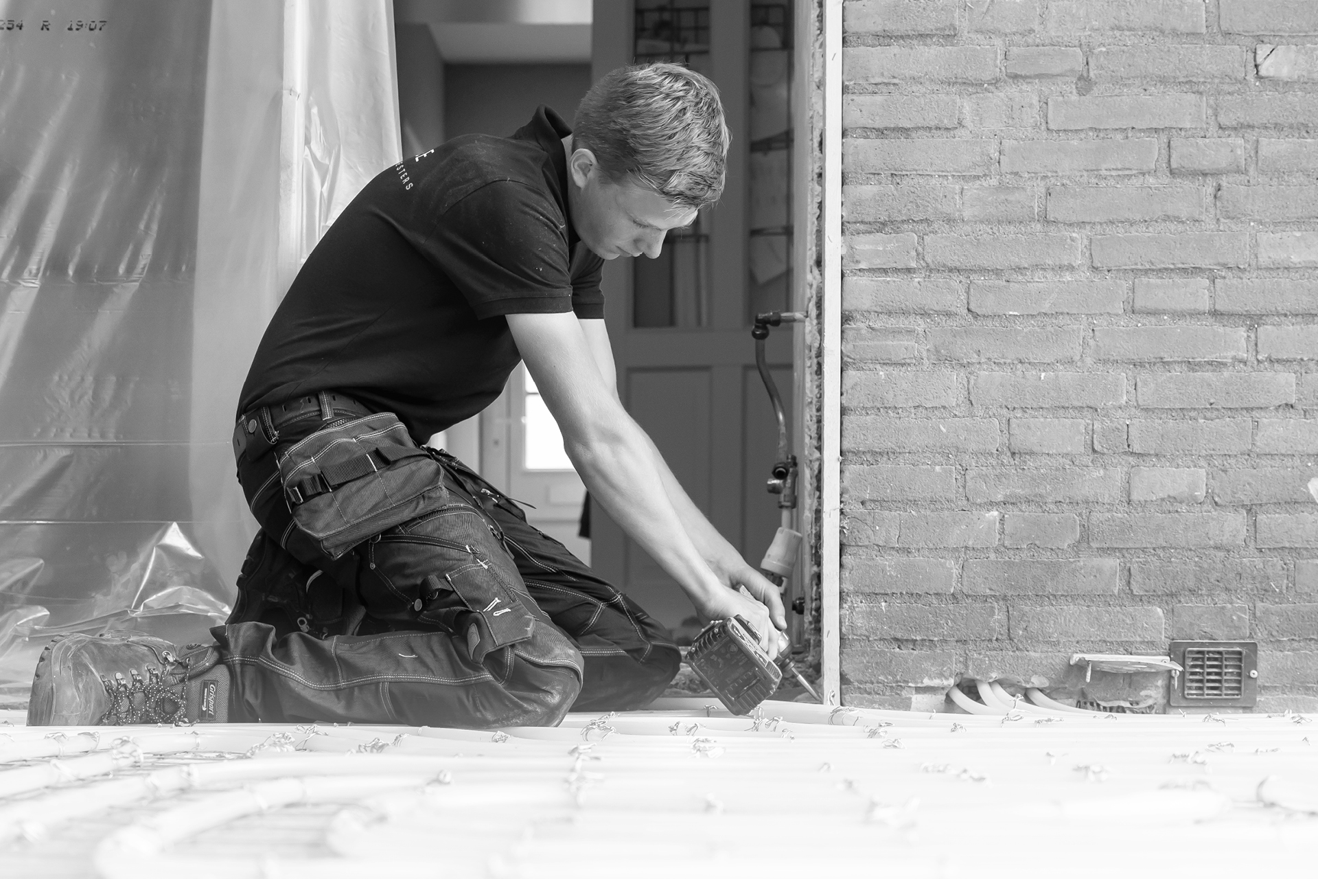 Een bouwvakker met een accuboormachine aan het werk, illustrerend voor het vakmanschap en de zorgvuldige manier van werken van Gelderse Bouwmeesters. Zowel in het veld als op kantoor bieden wij deskundig advies en betrokken ondersteuning voor al uw bouwprojecten.