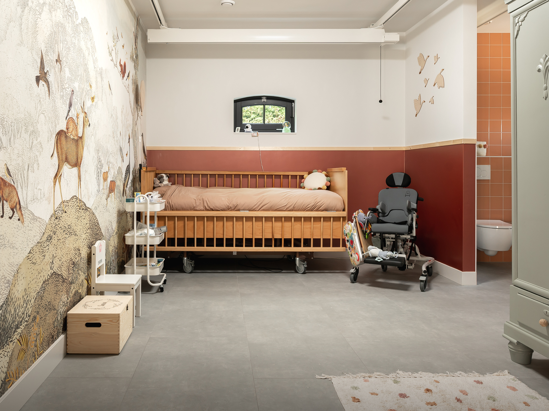 Slaapkamer met een bed en een rolstoel naast een toilet op de kamer, wat de toegankelijkheid en levensloopbestendigheid van de ruimte illustreert. Deze aanpassing biedt comfort en gemak voor senioren of mensen met een beperking.